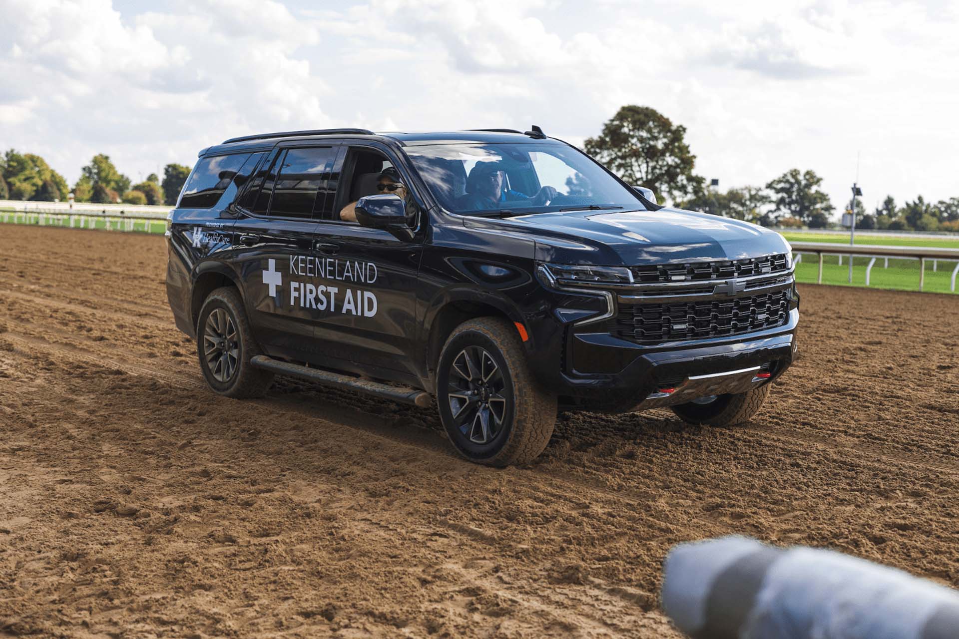 A picture of the Fastgalloptrack First Aid car on the dirt track. It is a large black Chevy SUV.